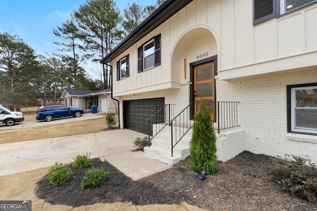 view of exterior entry with driveway, a garage, board and batten siding, and brick siding