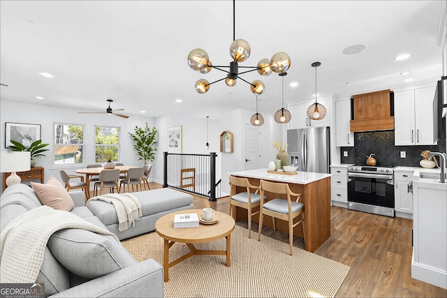 living area with ceiling fan with notable chandelier, light wood-type flooring, and recessed lighting