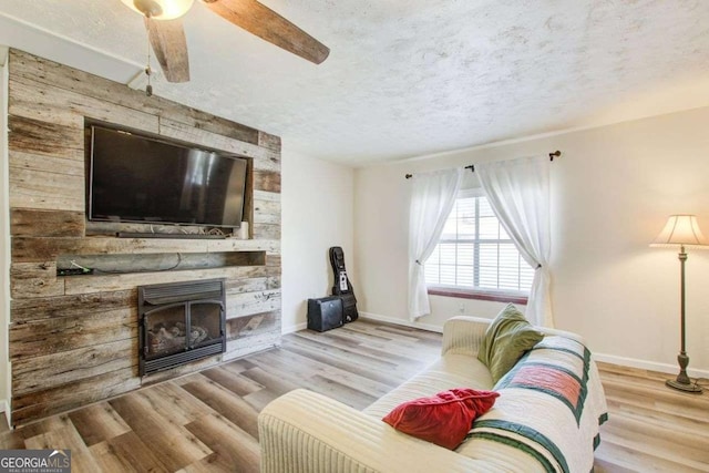 living room featuring a fireplace, light hardwood / wood-style flooring, a textured ceiling, and ceiling fan