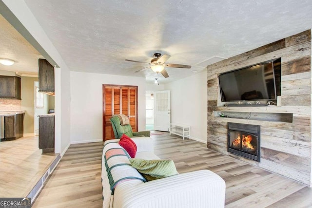 living room featuring a textured ceiling, ceiling fan, a fireplace, and light hardwood / wood-style flooring