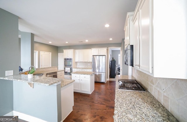 kitchen featuring white cabinetry, stainless steel appliances, kitchen peninsula, light stone countertops, and a breakfast bar area