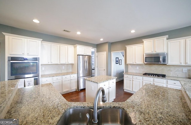 kitchen featuring appliances with stainless steel finishes, sink, light stone counters, and a center island