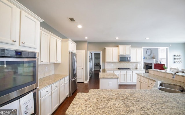 kitchen featuring a kitchen island, light stone countertops, sink, tasteful backsplash, and appliances with stainless steel finishes