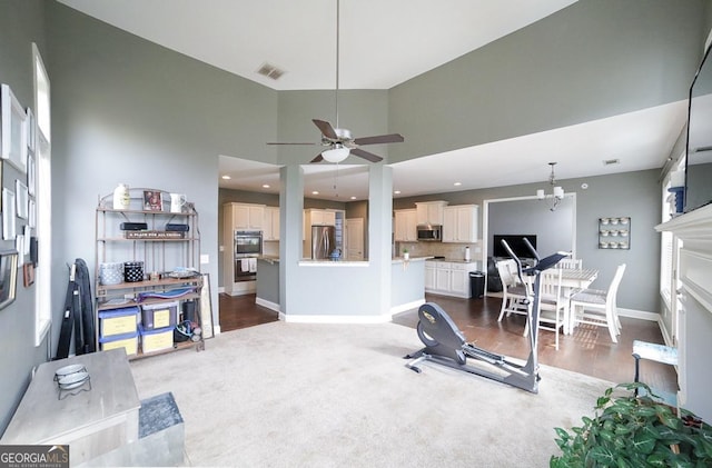 exercise room featuring ceiling fan with notable chandelier, dark carpet, and a high ceiling