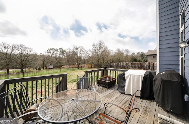 wooden terrace featuring a lawn, a grill, and an outdoor fire pit