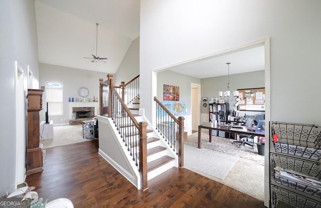 stairway featuring ceiling fan with notable chandelier, high vaulted ceiling, and wood-type flooring