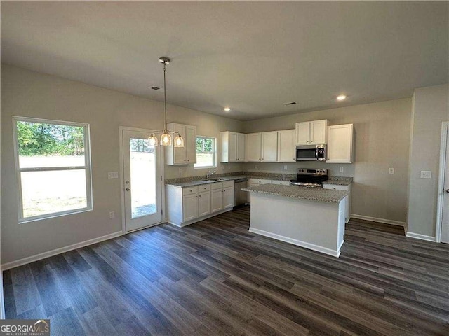 kitchen featuring dark wood finished floors, stainless steel appliances, white cabinets, a kitchen island, and baseboards