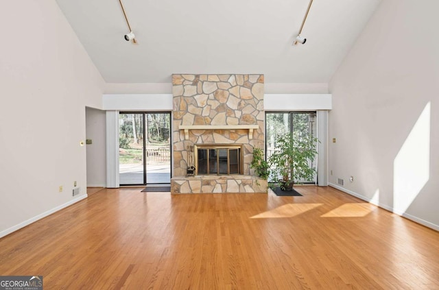 unfurnished living room featuring hardwood / wood-style flooring, high vaulted ceiling, rail lighting, and a stone fireplace