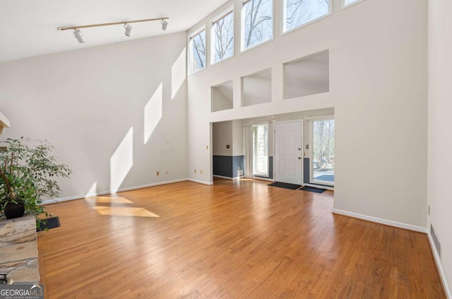 unfurnished living room with hardwood / wood-style flooring, track lighting, and a towering ceiling