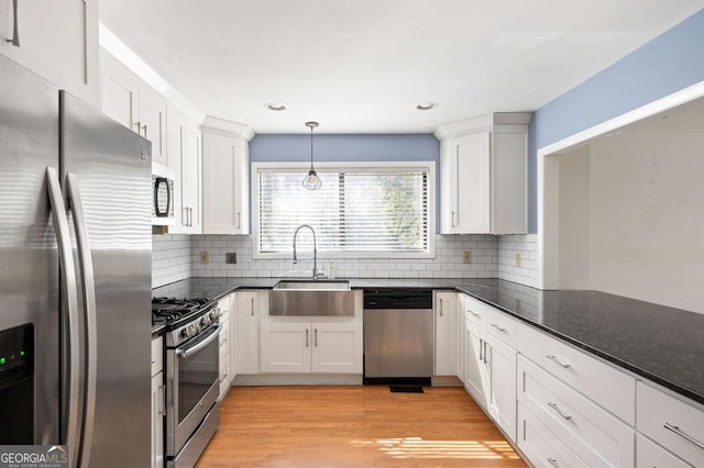 kitchen featuring sink, white cabinets, stainless steel appliances, and hanging light fixtures