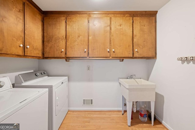 clothes washing area featuring independent washer and dryer, cabinets, and light hardwood / wood-style floors