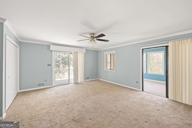 carpeted empty room with ceiling fan, ornamental molding, and plenty of natural light