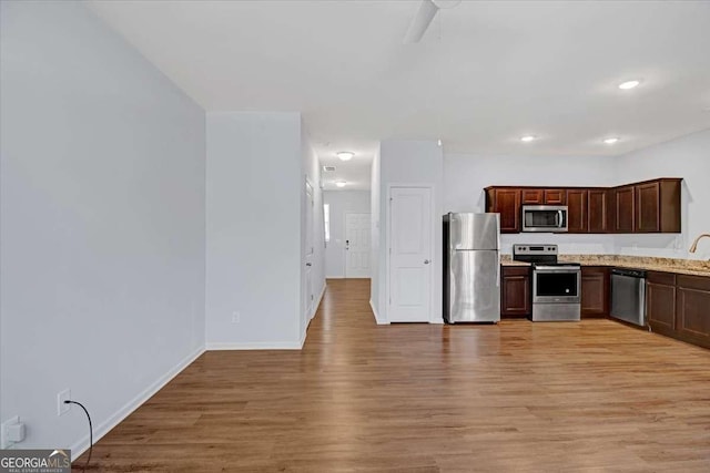 kitchen with appliances with stainless steel finishes, dark brown cabinetry, light stone counters, and light hardwood / wood-style flooring