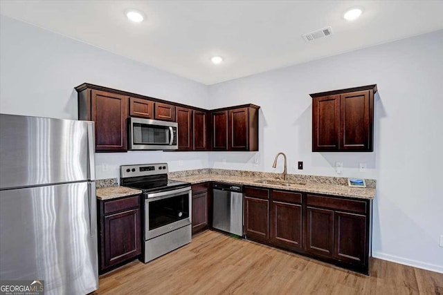 kitchen featuring appliances with stainless steel finishes, sink, light stone counters, and light wood-type flooring