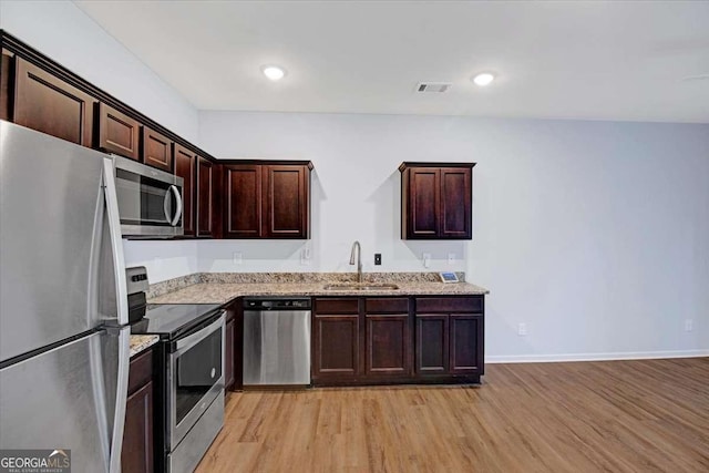 kitchen featuring dark brown cabinets, stainless steel appliances, light stone counters, light hardwood / wood-style floors, and sink