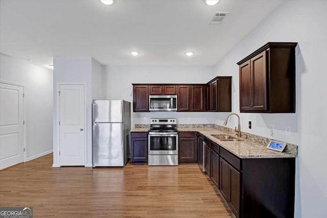 kitchen featuring sink, light hardwood / wood-style floors, stainless steel appliances, and light stone counters