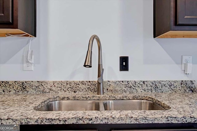 interior details with dark brown cabinetry, light stone counters, and sink