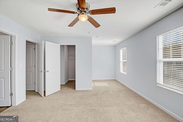 unfurnished bedroom featuring a walk in closet, ceiling fan, a closet, and light colored carpet