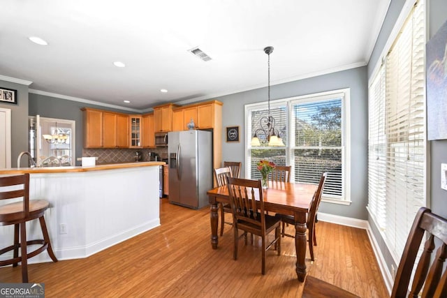 kitchen featuring light wood-type flooring, appliances with stainless steel finishes, crown molding, and pendant lighting