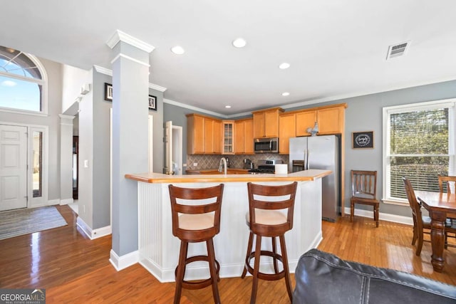 kitchen with decorative backsplash, stainless steel appliances, ornate columns, and hardwood / wood-style floors