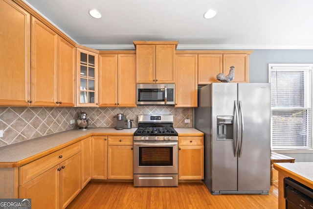 kitchen featuring appliances with stainless steel finishes, ornamental molding, decorative backsplash, and light hardwood / wood-style flooring