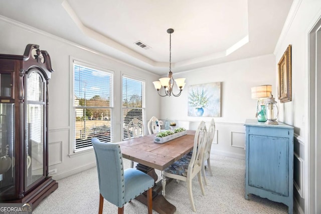 carpeted dining area featuring a tray ceiling, ornamental molding, and a notable chandelier