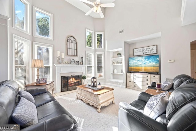 living room featuring built in features, light carpet, a towering ceiling, and ceiling fan