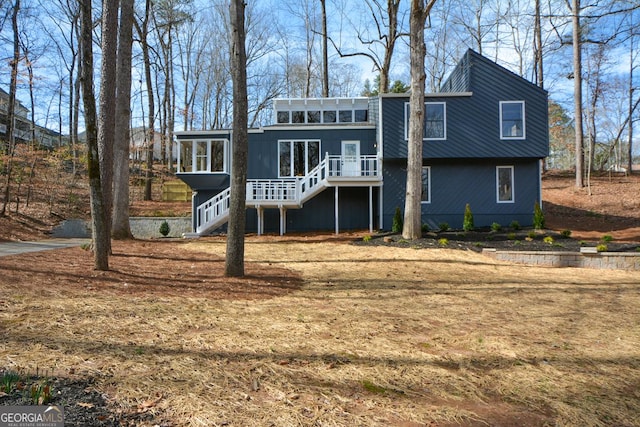 rear view of house with stairway, a wooden deck, and a sunroom