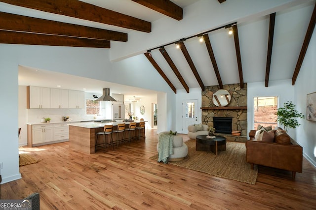 living room featuring light wood finished floors, high vaulted ceiling, a stone fireplace, and baseboards