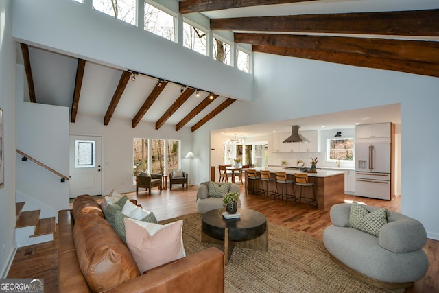 living room with light wood-style flooring, stairs, high vaulted ceiling, and beam ceiling