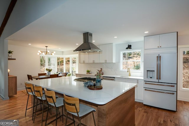 kitchen featuring decorative light fixtures, paneled built in fridge, white cabinetry, a kitchen island, and island range hood