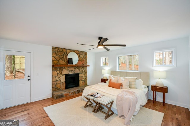 bedroom with ceiling fan, baseboards, wood finished floors, and a stone fireplace