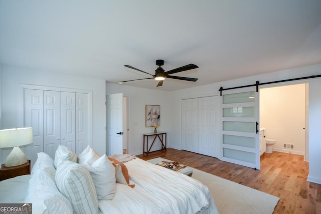 bedroom featuring a barn door, baseboards, visible vents, light wood-style flooring, and multiple closets