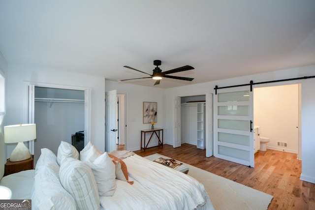 bedroom featuring a barn door, baseboards, ceiling fan, light wood-style flooring, and multiple closets