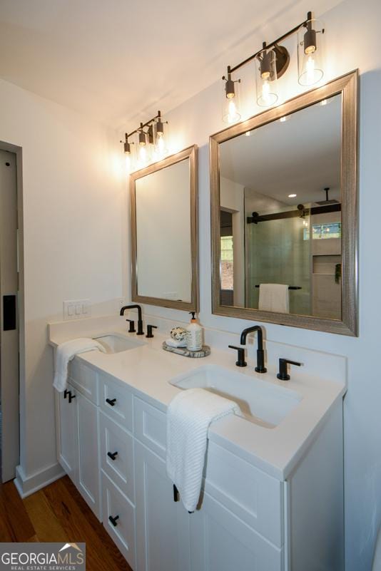 bathroom featuring double vanity, wood finished floors, a sink, and a shower stall