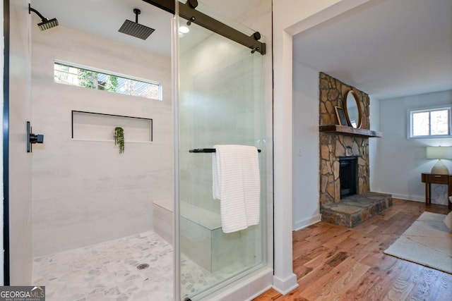 bathroom with a stall shower, a fireplace, wood finished floors, and baseboards