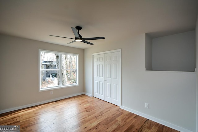 unfurnished bedroom with a closet, ceiling fan, light wood-style flooring, and baseboards