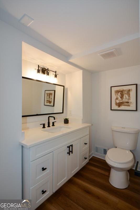 half bath featuring toilet, vanity, wood finished floors, and visible vents