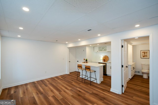 kitchen featuring dark wood-style flooring, a kitchen island, a kitchen breakfast bar, white cabinets, and light countertops