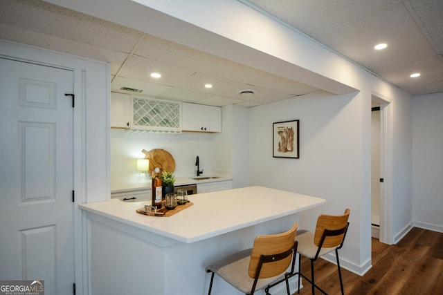 kitchen with white cabinets, a kitchen breakfast bar, a peninsula, light countertops, and a sink