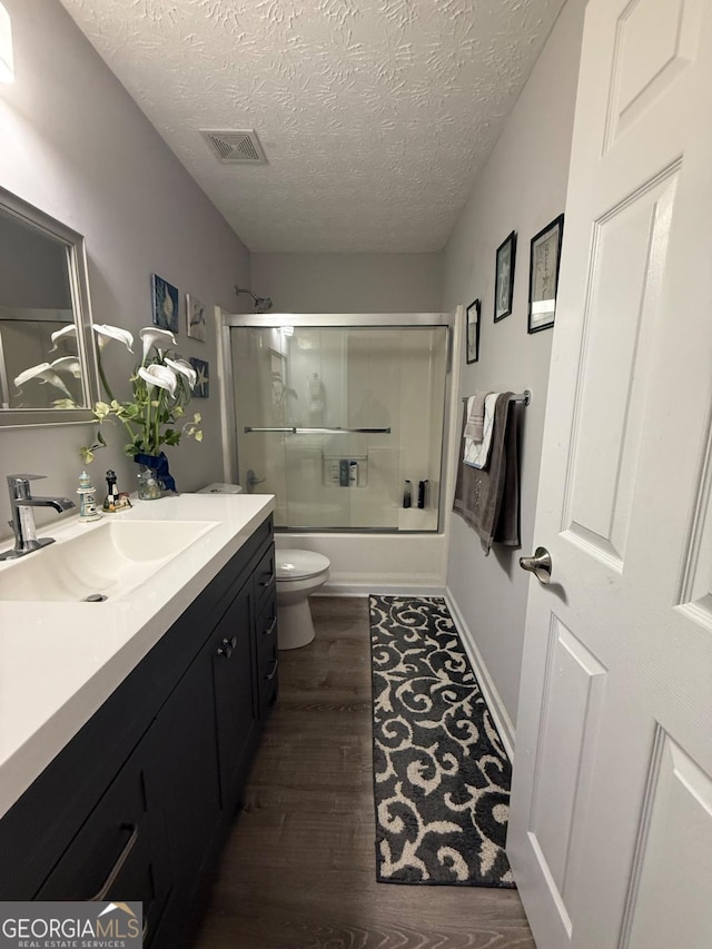 full bathroom featuring hardwood / wood-style flooring, toilet, shower / bath combination with glass door, a textured ceiling, and vanity