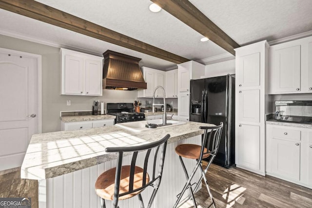 kitchen featuring a center island with sink, a kitchen breakfast bar, custom range hood, black appliances, and white cabinets