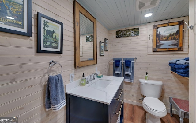 bathroom with wood-type flooring, toilet, wooden walls, wood ceiling, and vanity