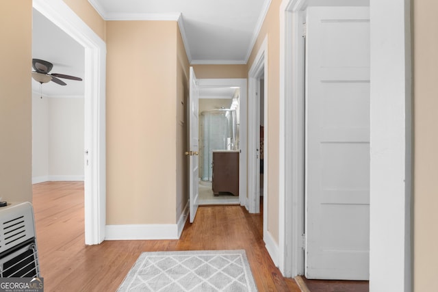 hallway featuring heating unit, baseboards, crown molding, and wood finished floors