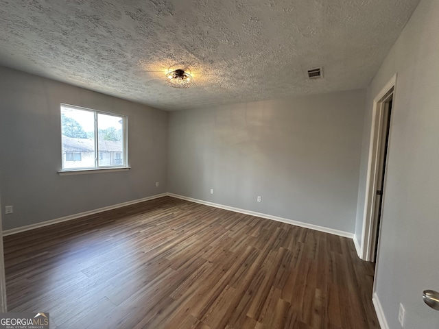 spare room featuring baseboards, visible vents, dark wood finished floors, and a textured ceiling