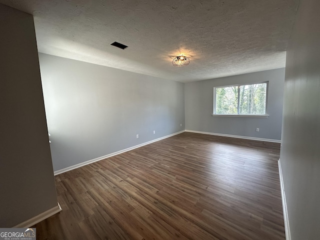 empty room with dark wood-type flooring, visible vents, a textured ceiling, and baseboards