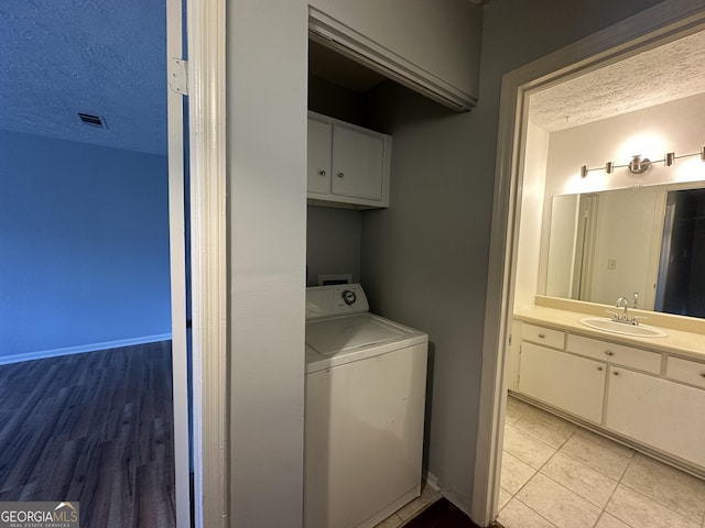 laundry room featuring a textured ceiling, a sink, visible vents, cabinet space, and washer / clothes dryer