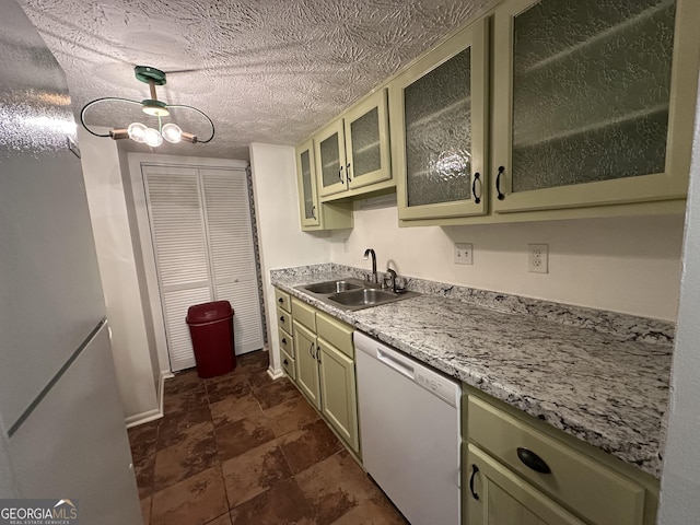 kitchen with a textured ceiling, white dishwasher, a sink, baseboards, and glass insert cabinets