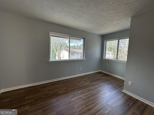 empty room featuring dark wood-style floors, a textured ceiling, and baseboards