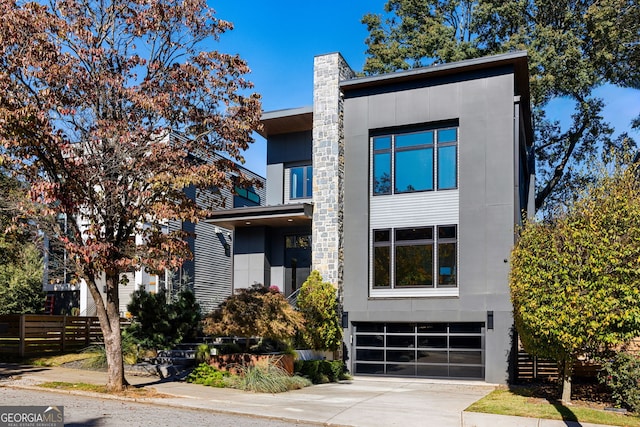 modern home featuring a chimney, concrete driveway, a garage, and fence